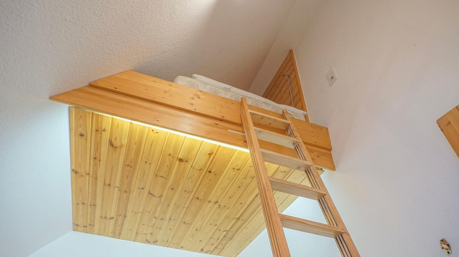 A bedroom with a double bed on a wooden platform with ladder and lighting.