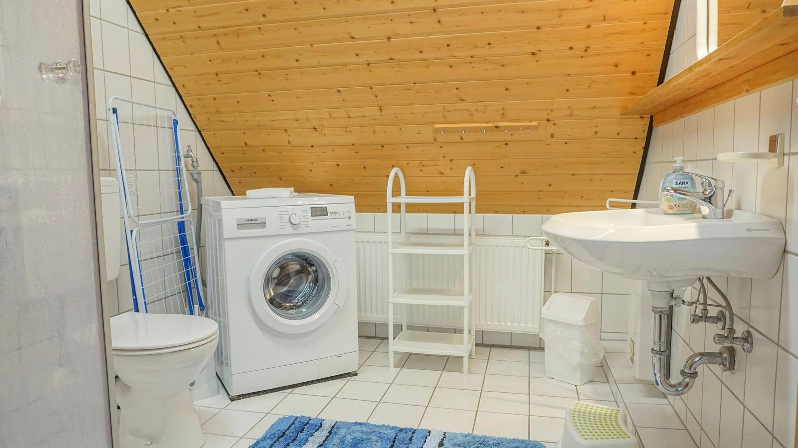 Bathroom with washing machine, sink, and toilet under wooden ceiling.