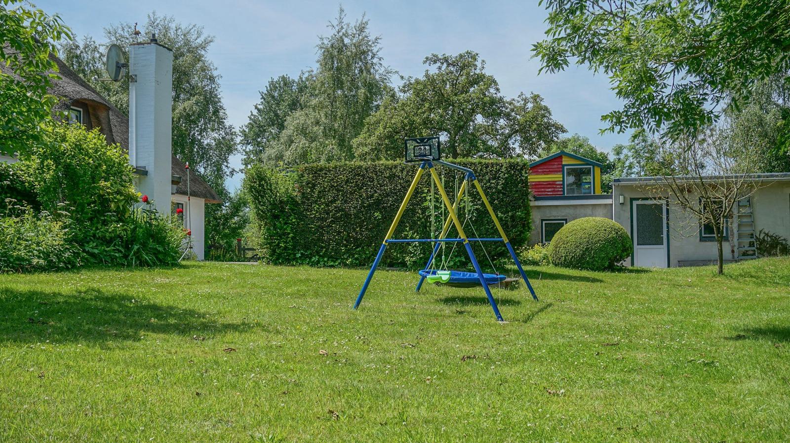A blue and yellow swing set stands on a green lawn in front of a garden shed.