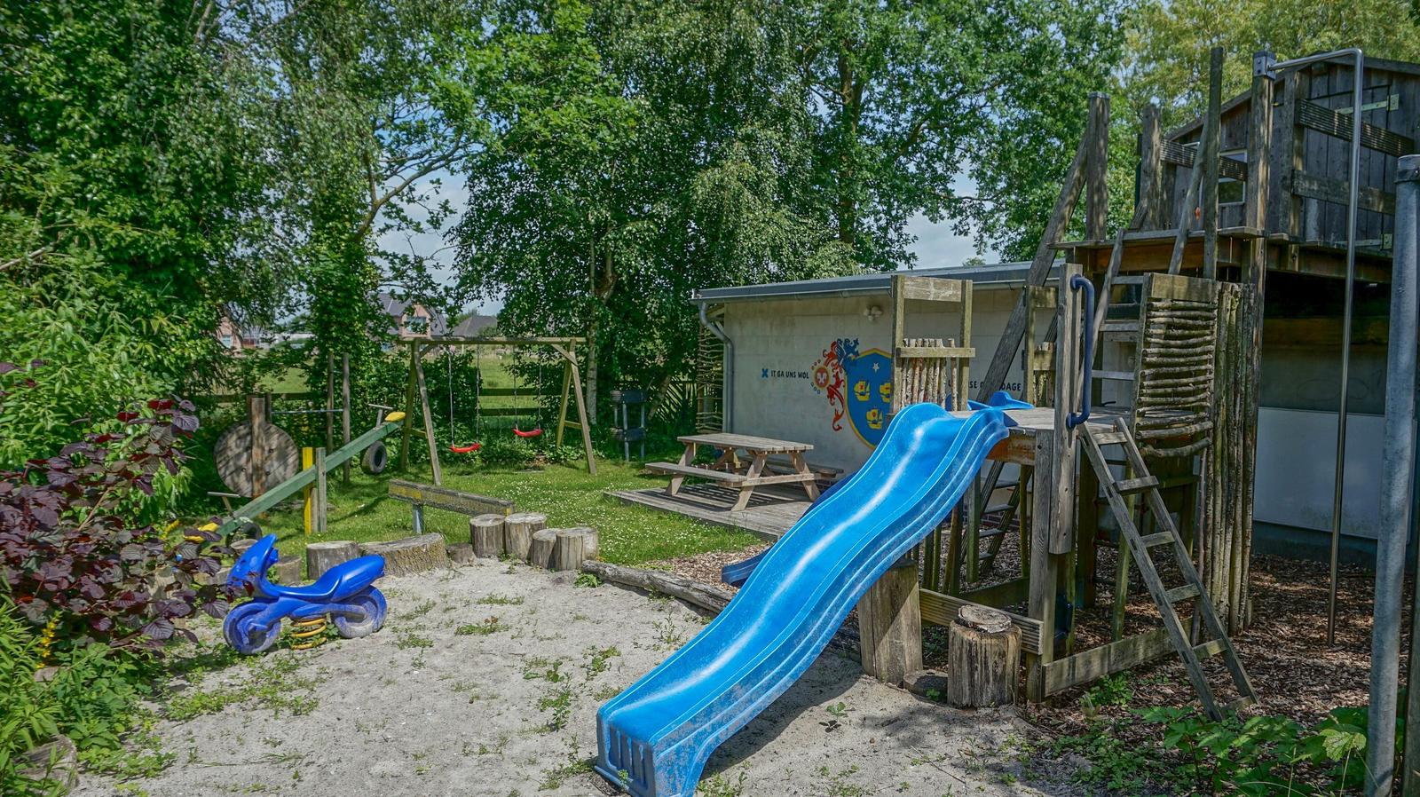 Backyard with playground, slide, and swing. Green lawn and wooden play equipment.