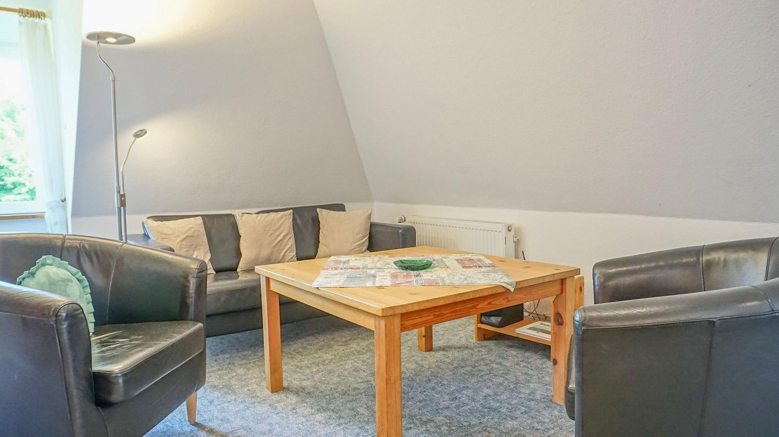 Living room with sofa, two armchairs, and wooden table under sloped ceiling