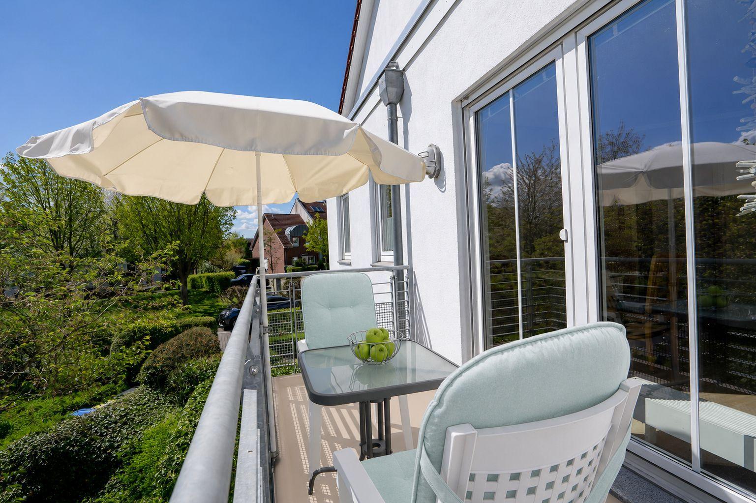 Terrasse mit Tisch, zwei Stühlen und Sonnenschirm. Blick auf grüne Umgebung.