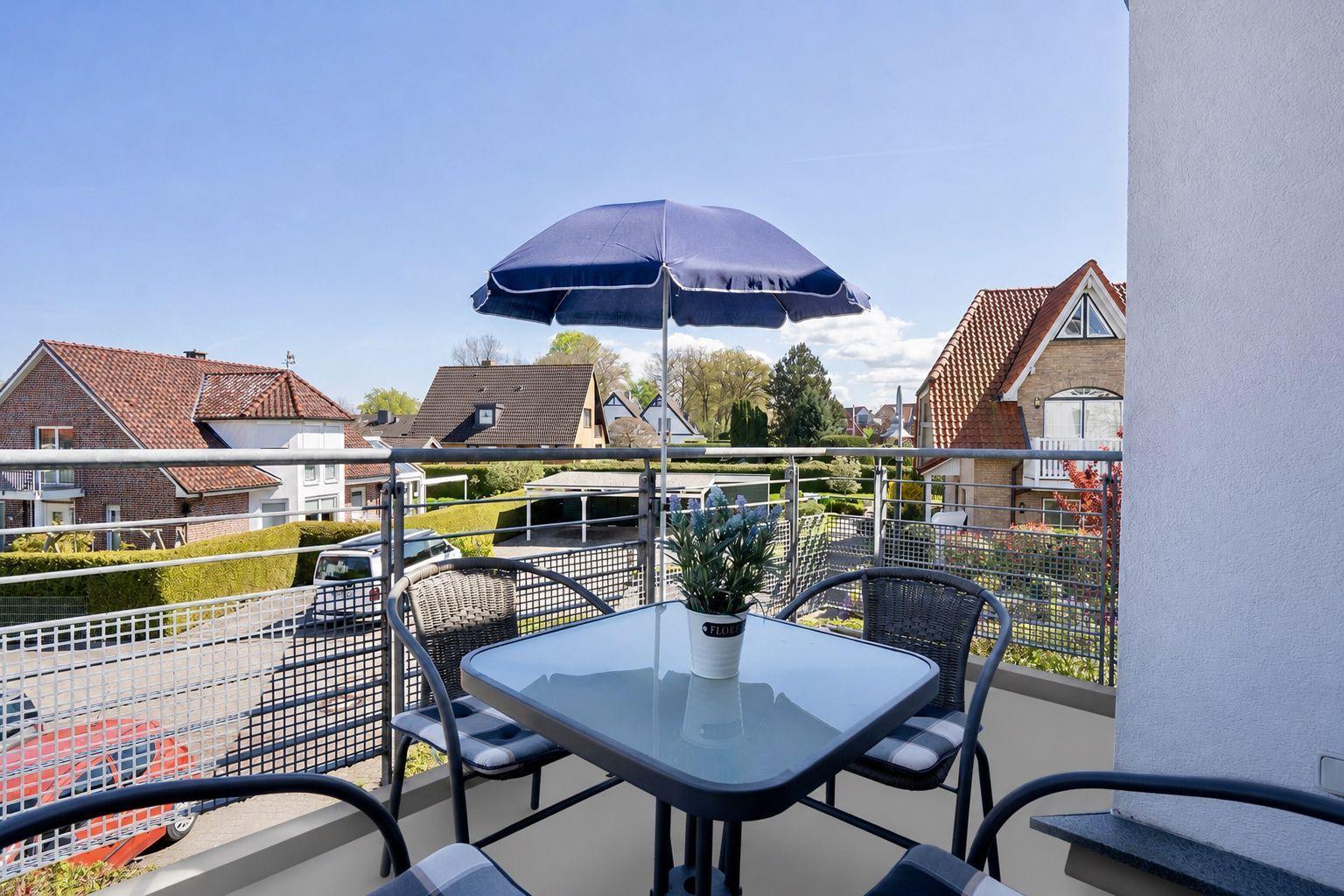Balcony with table, chairs, and umbrella overlooking residential area.