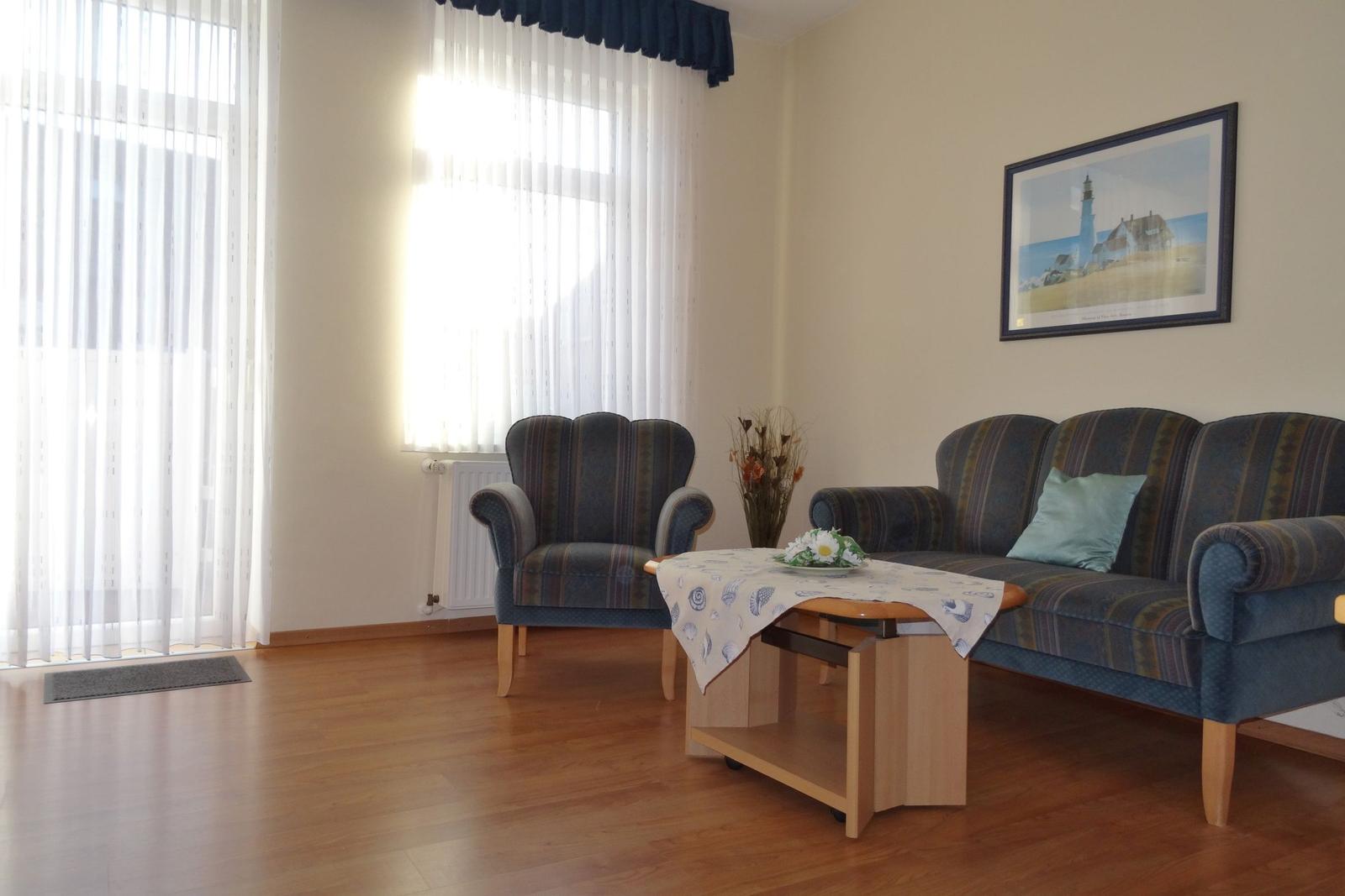 Wohnzimmer mit Sofa, Sessel und Tisch. Fenster mit Vorhängen und Wandbild.