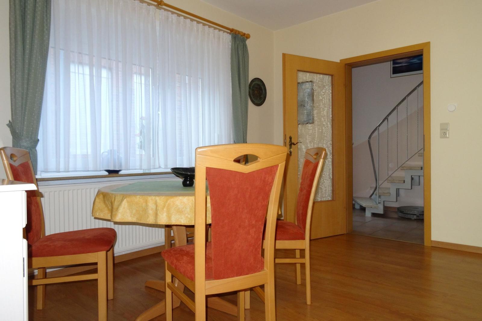 Esszimmer mit runden Tisch und Stühlen, Fenster mit Vorhängen und Tür zum Flur.