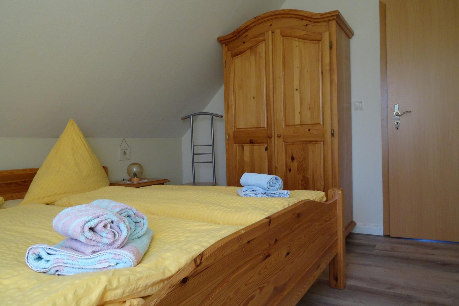 Schlafzimmer mit Holzbett, Kleiderschrank und gefalteten Handtüchern.