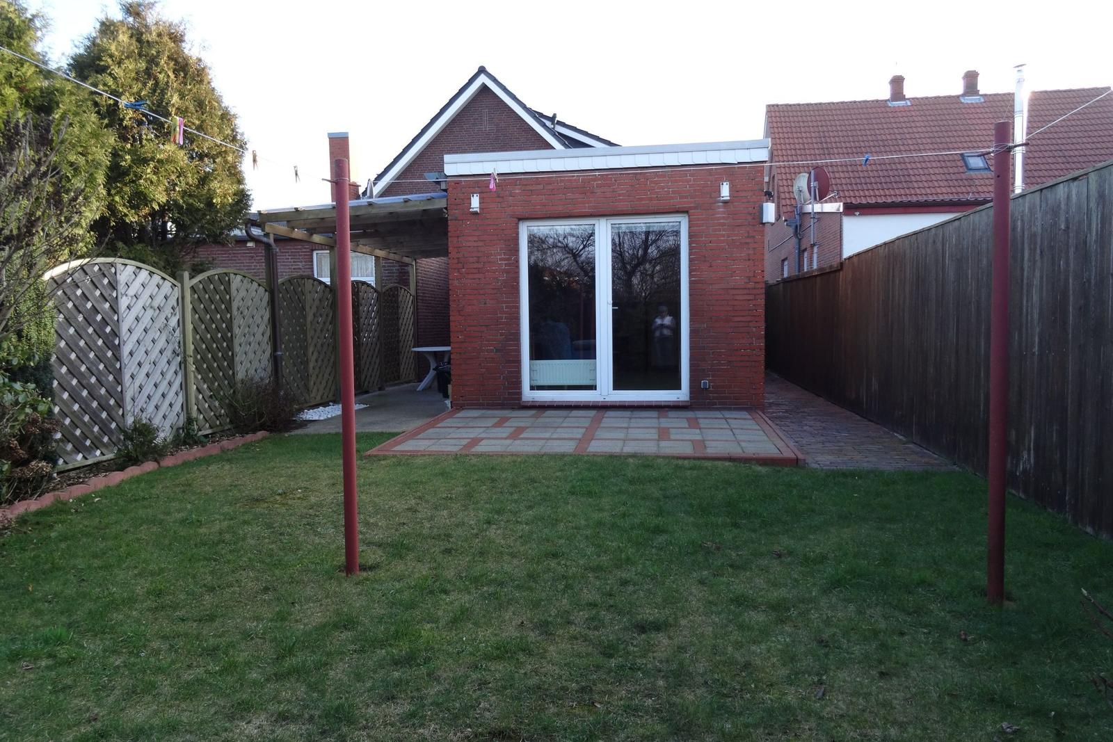 Roter Backsteinbau mit Glasfront und gepflasterter Terrasse im Garten.