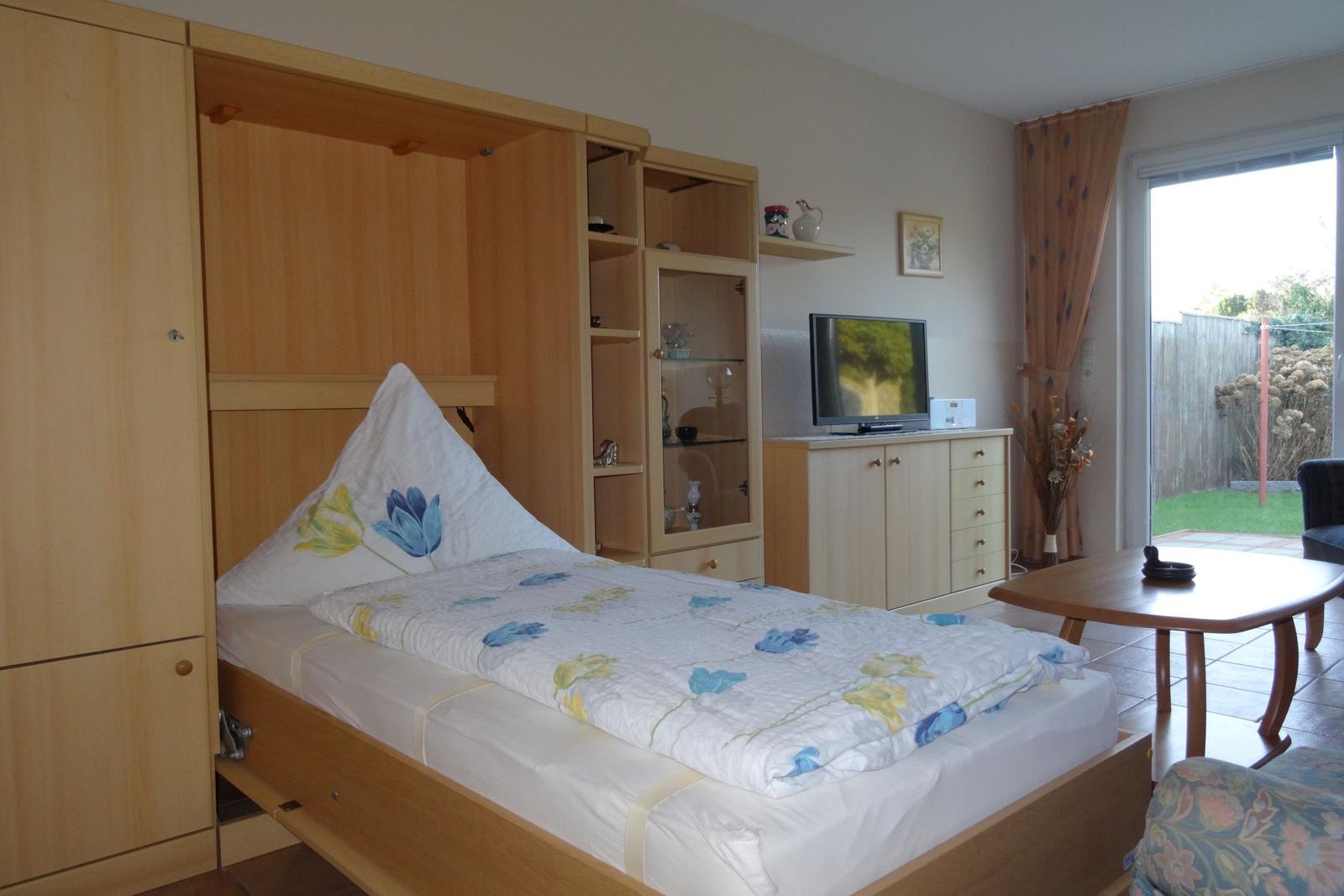 Schlafzimmer mit ausziehbarer Bettanlage, Fernseher und Blick auf den Garten.