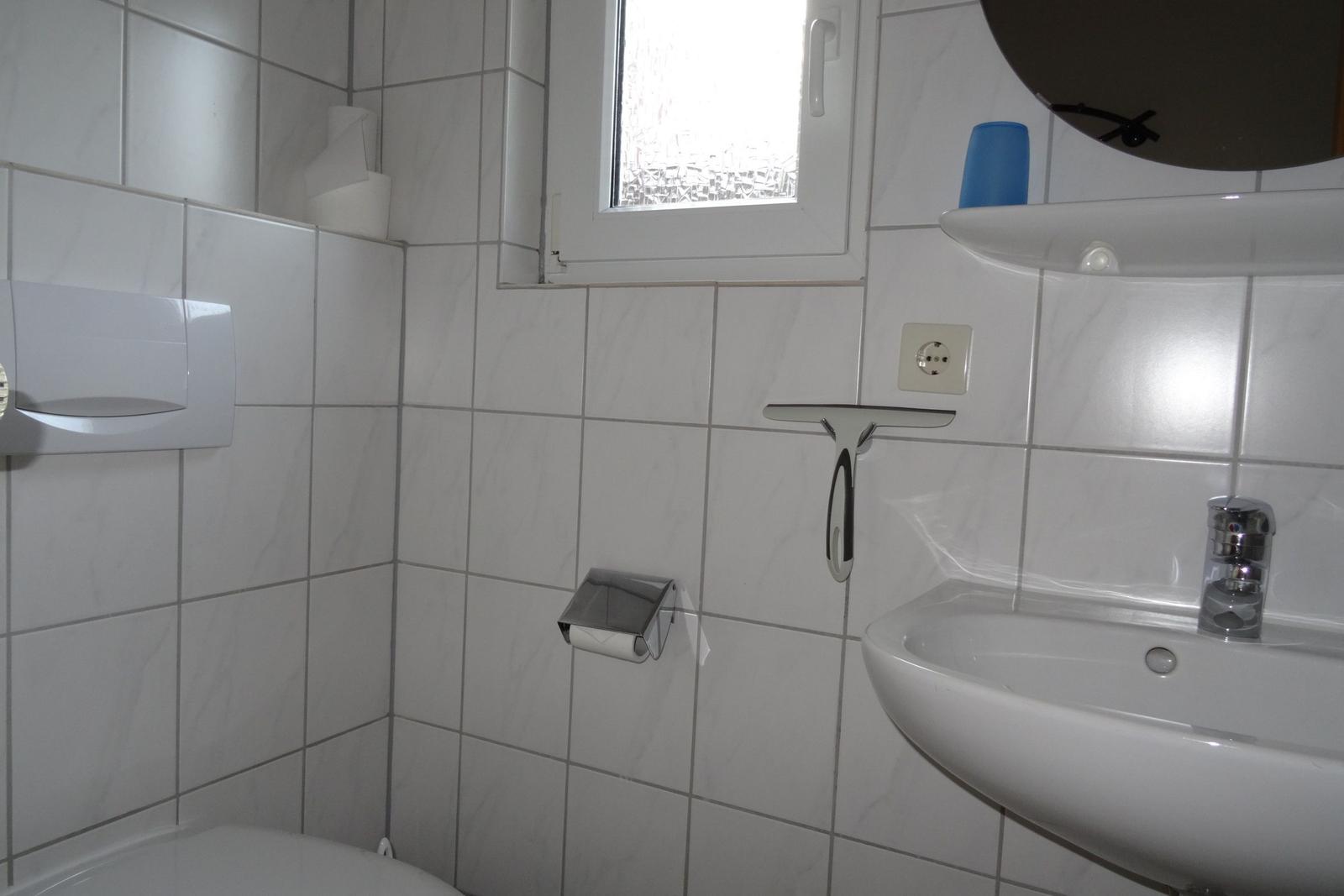 Badezimmer mit Waschbecken, Spiegel, Toilette und Fenster.