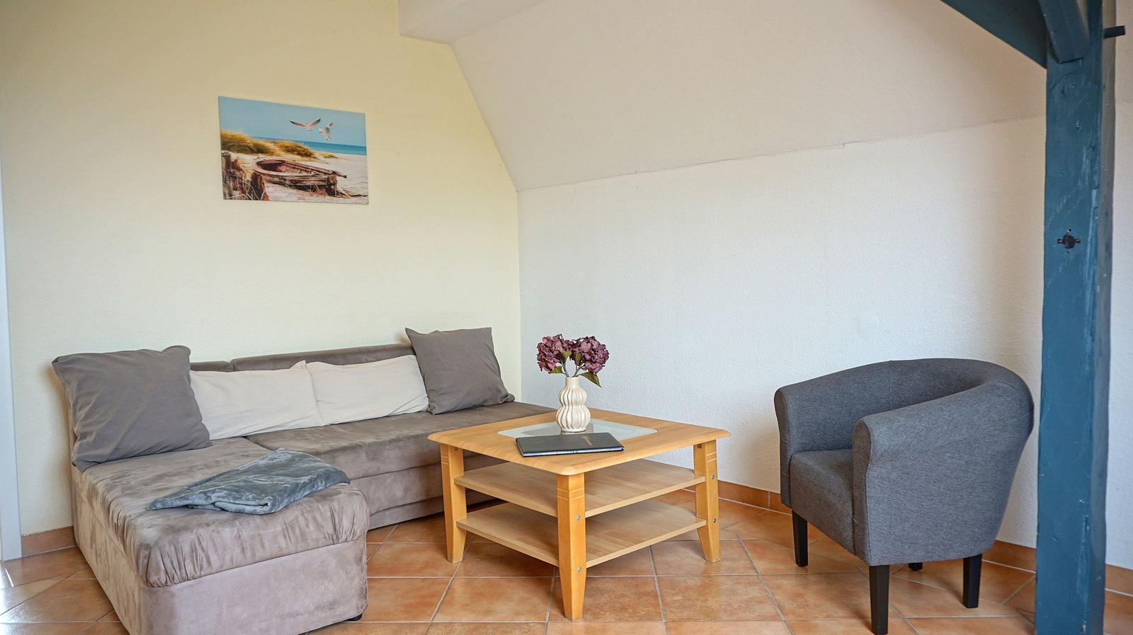 Wohnzimmer mit Sofa, Sessel und Tisch. Wandbild zeigt Strand. Holzfußboden und Holzrahmen.