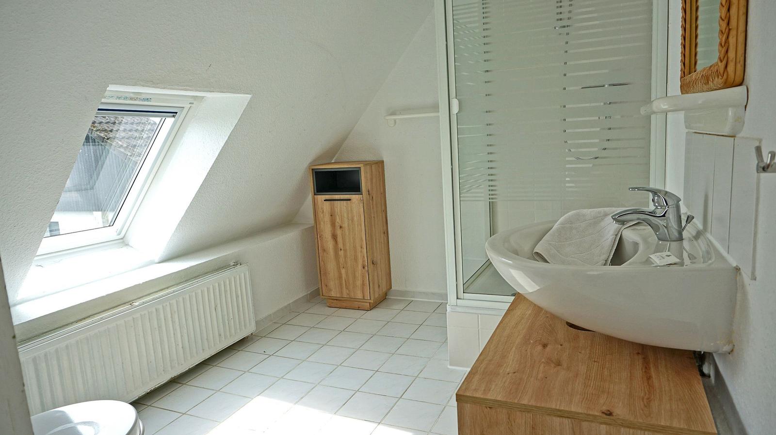 Badezimmer mit Dachfenster, Waschbecken auf Holzunterschrank und Dusche mit Glaswand.