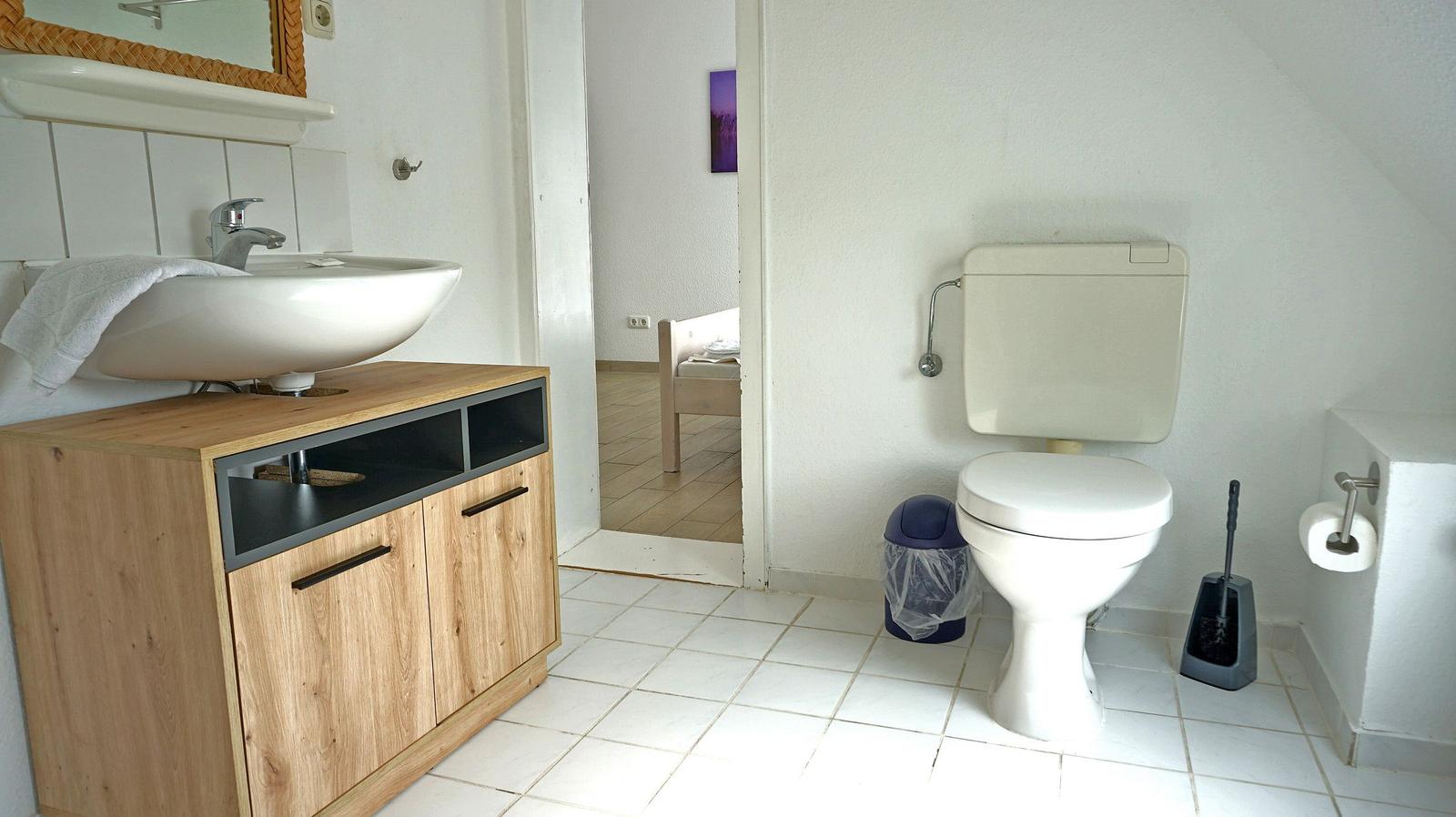 Badezimmer mit Waschbecken, Toilette und Spiegel. Holzunterschrank und Fliesenboden.