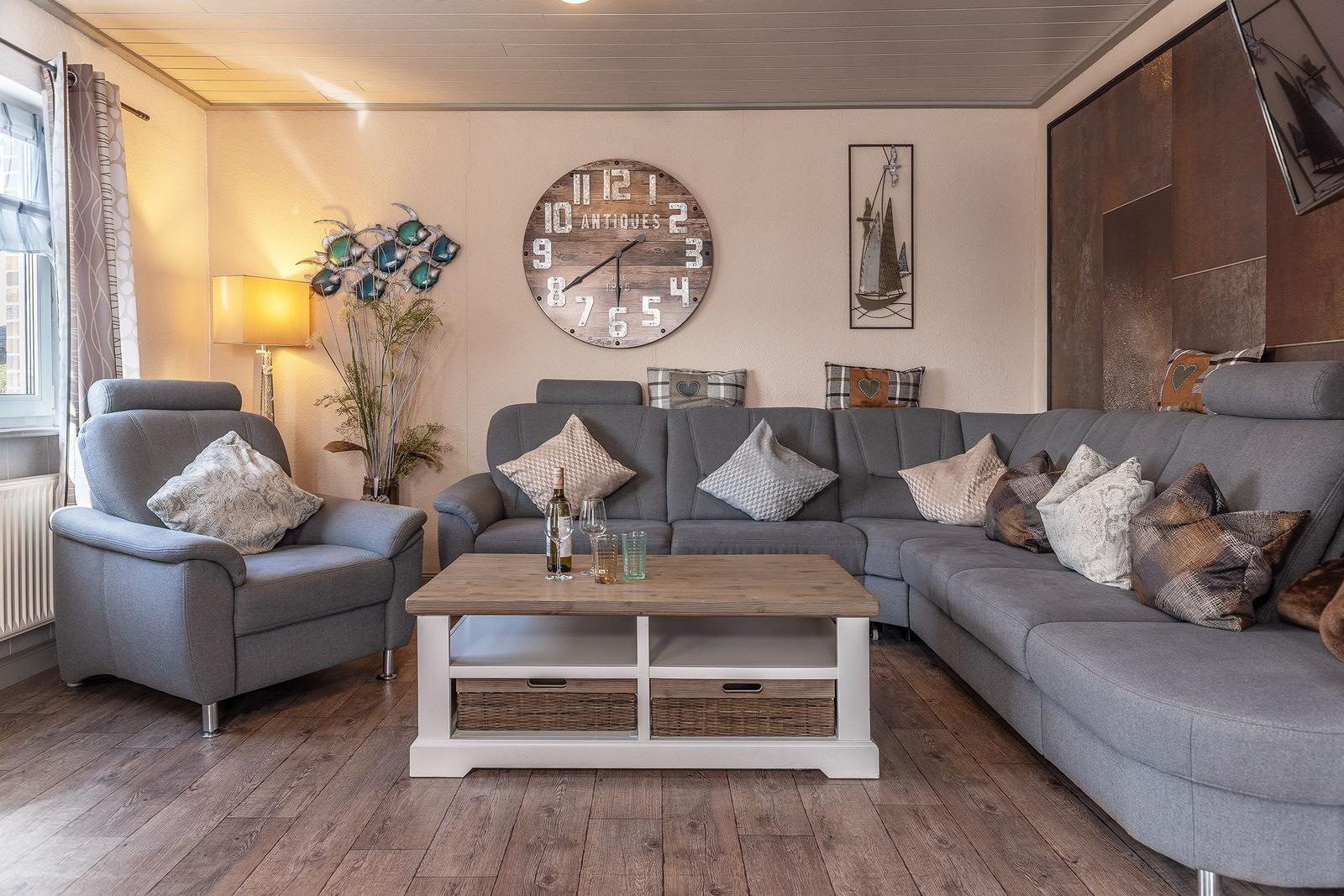 Wohnzimmer mit grauem Sofa, Holztisch und Wanduhr