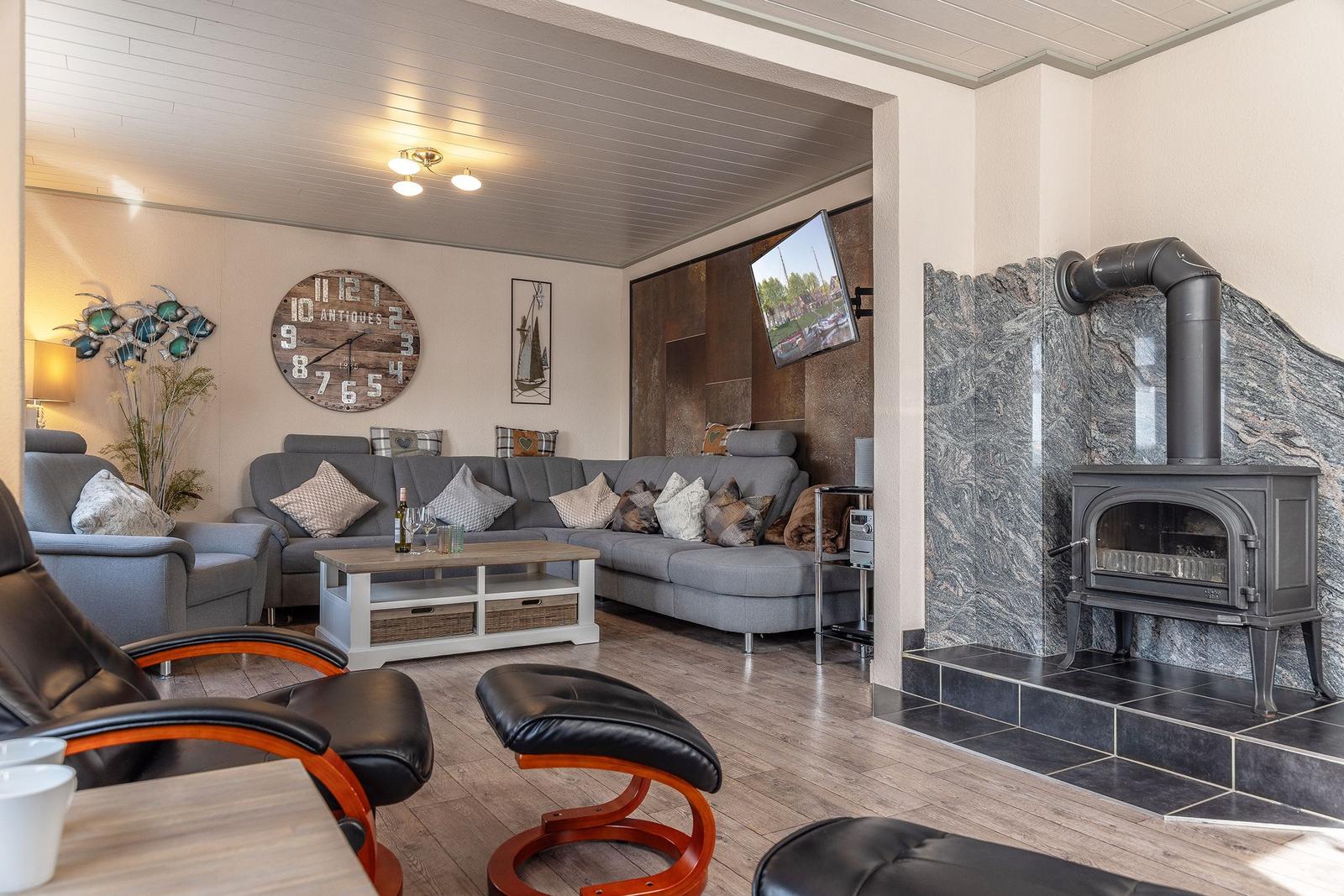 Wohnzimmer mit Sofa, Kamin und Wanduhr. Holzboden und Fernseher sichtbar.