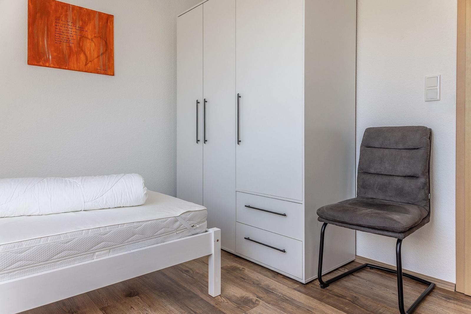 Schlafzimmer mit Bett, Kleiderschrank und Stuhl. Wandbild und Holzboden.