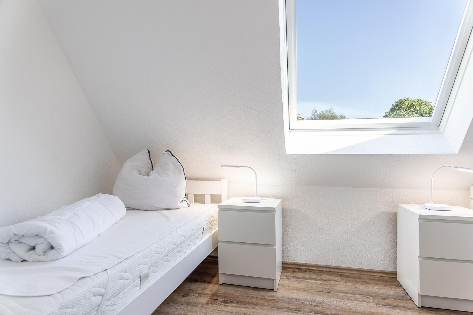 Schlafzimmer mit Dachschrägen, weißem Bett und zwei Nachttischen unter einem Dachfenster.