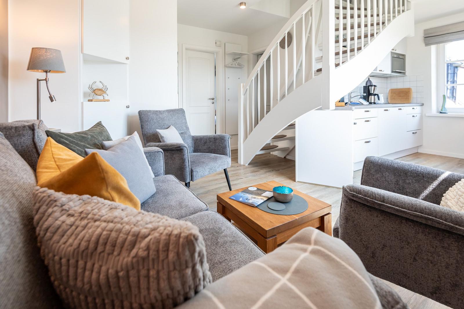 Wohnzimmer mit Sofa, Sessel und Küchenbereich unter einer Treppe.