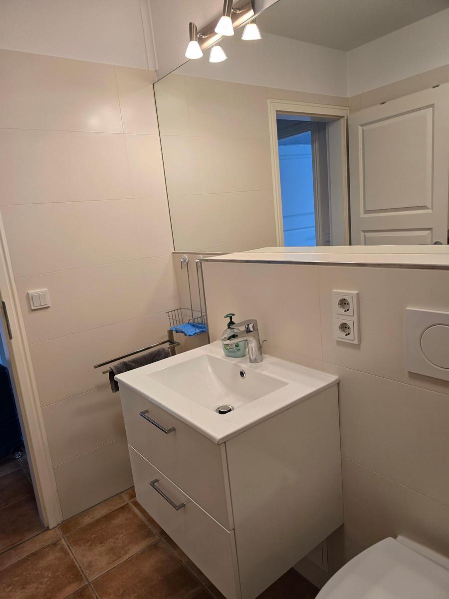 Badezimmer mit Waschbecken, Spiegel und Toilette. Fliesen und weiße Möbel.