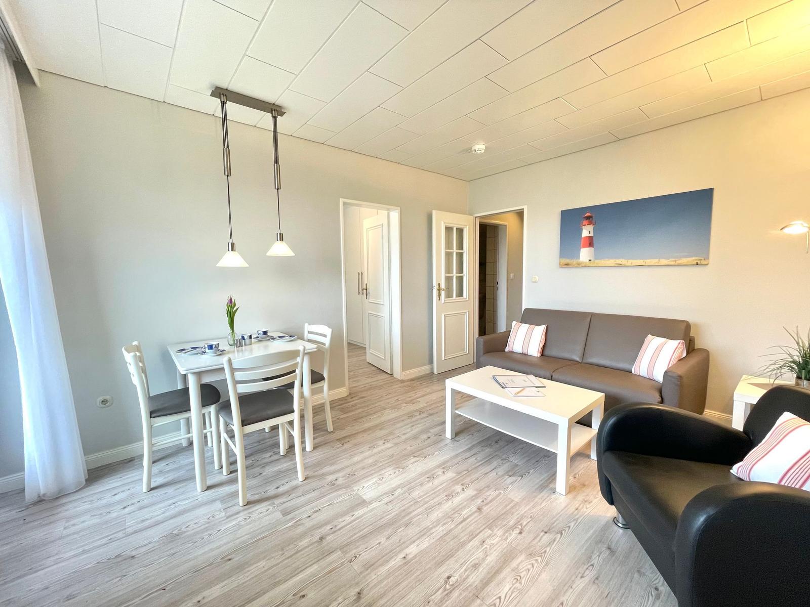 Wohn- und Essbereich mit Sofa, Sitzbank, Esstisch und Wandbild mit Leuchtturm.