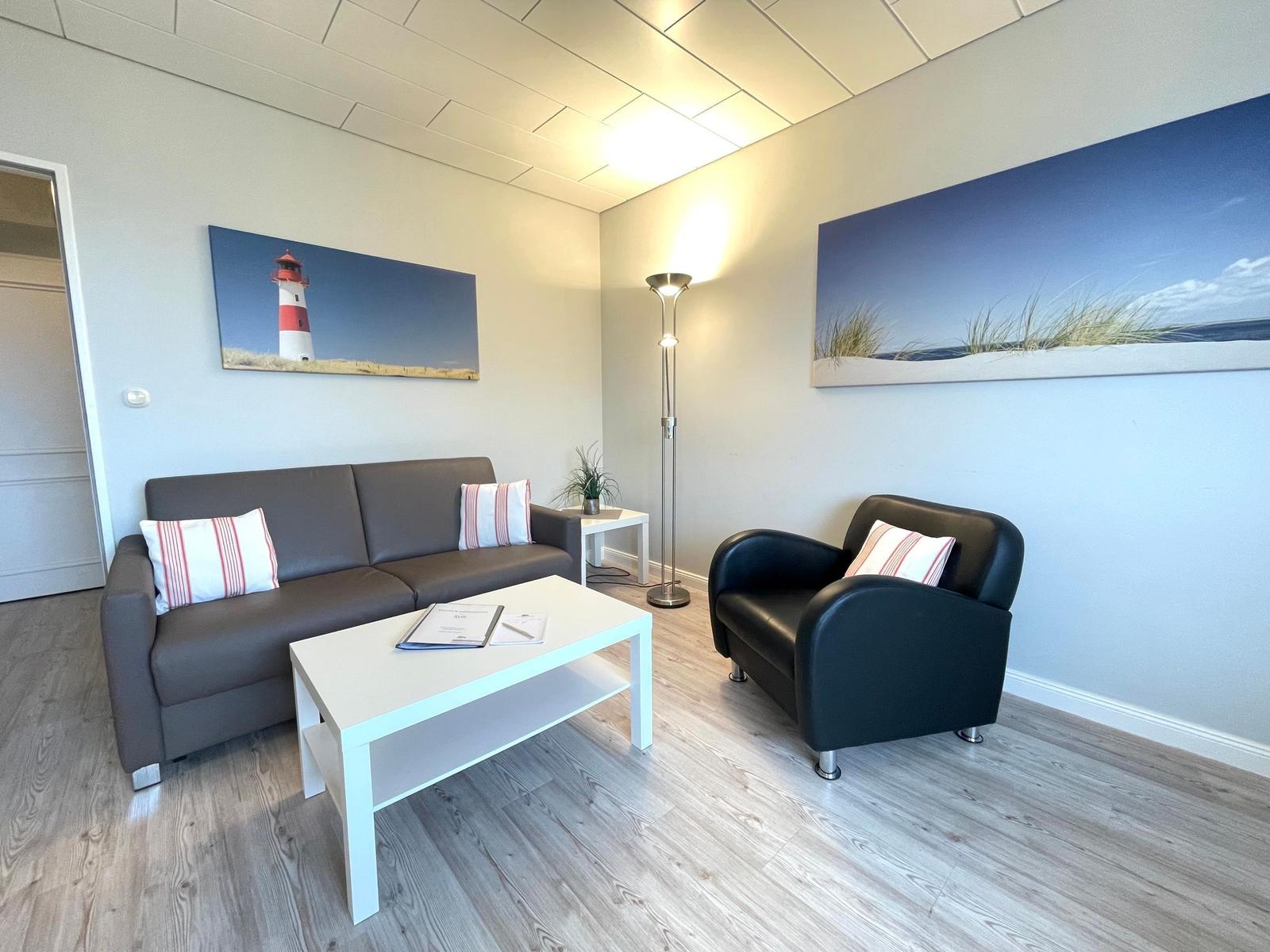 Wohnzimmer mit Sofa, Sessel, Tisch und Wandbildern