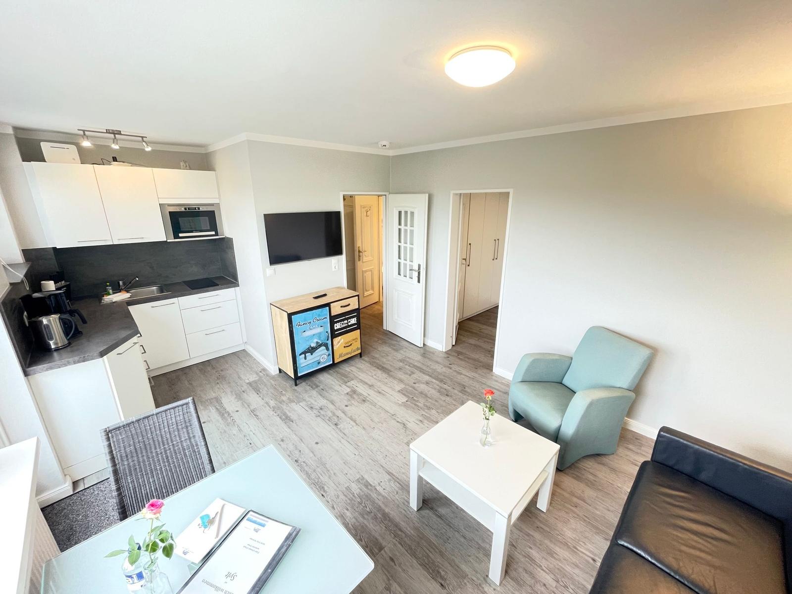 Wohnung mit Küche, Wohnbereich, Sofa, Sessel und Fernseher.