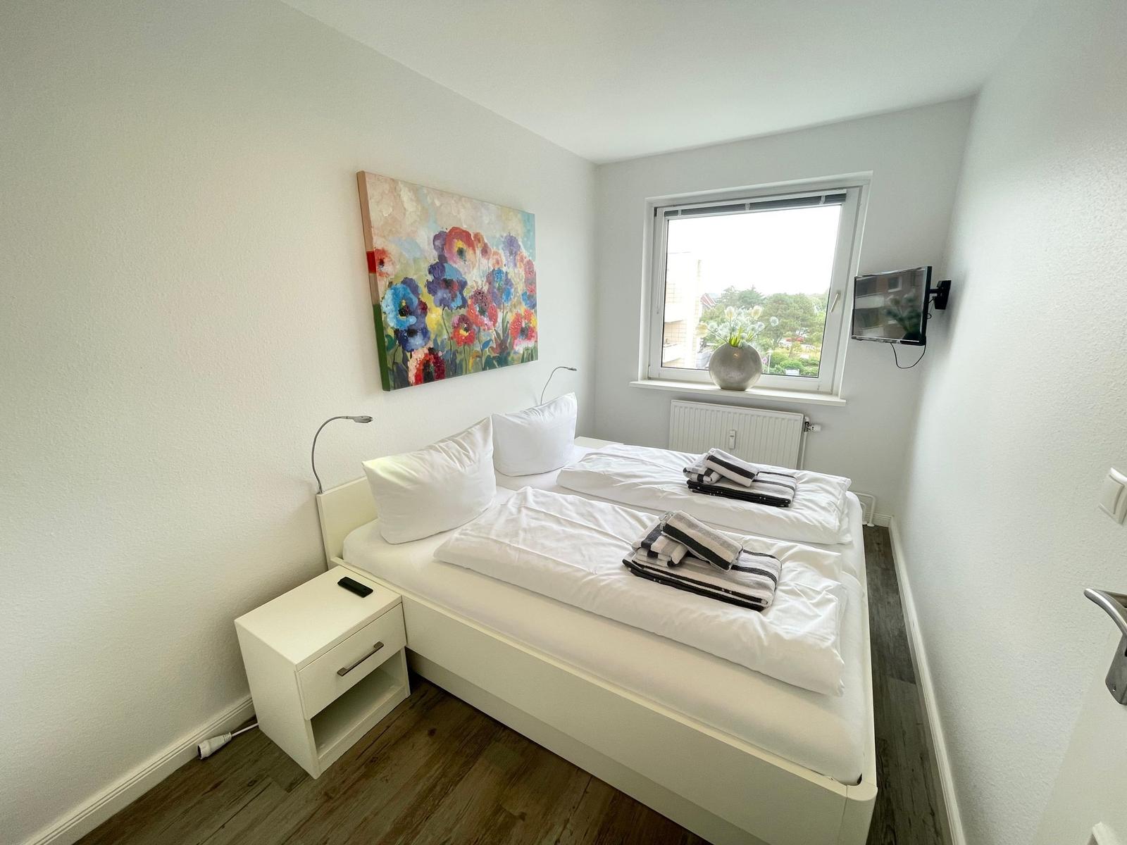 Schlafzimmer mit Doppelbett, Fenster, Wandbild und Nachttisch.
