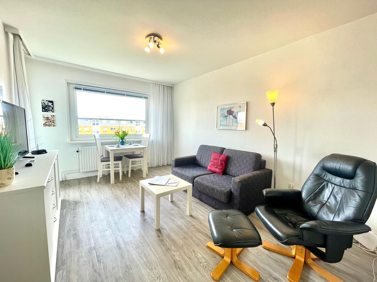 Wohnzimmer mit Sofa, Essbereich und schwarzer Relaxliege.