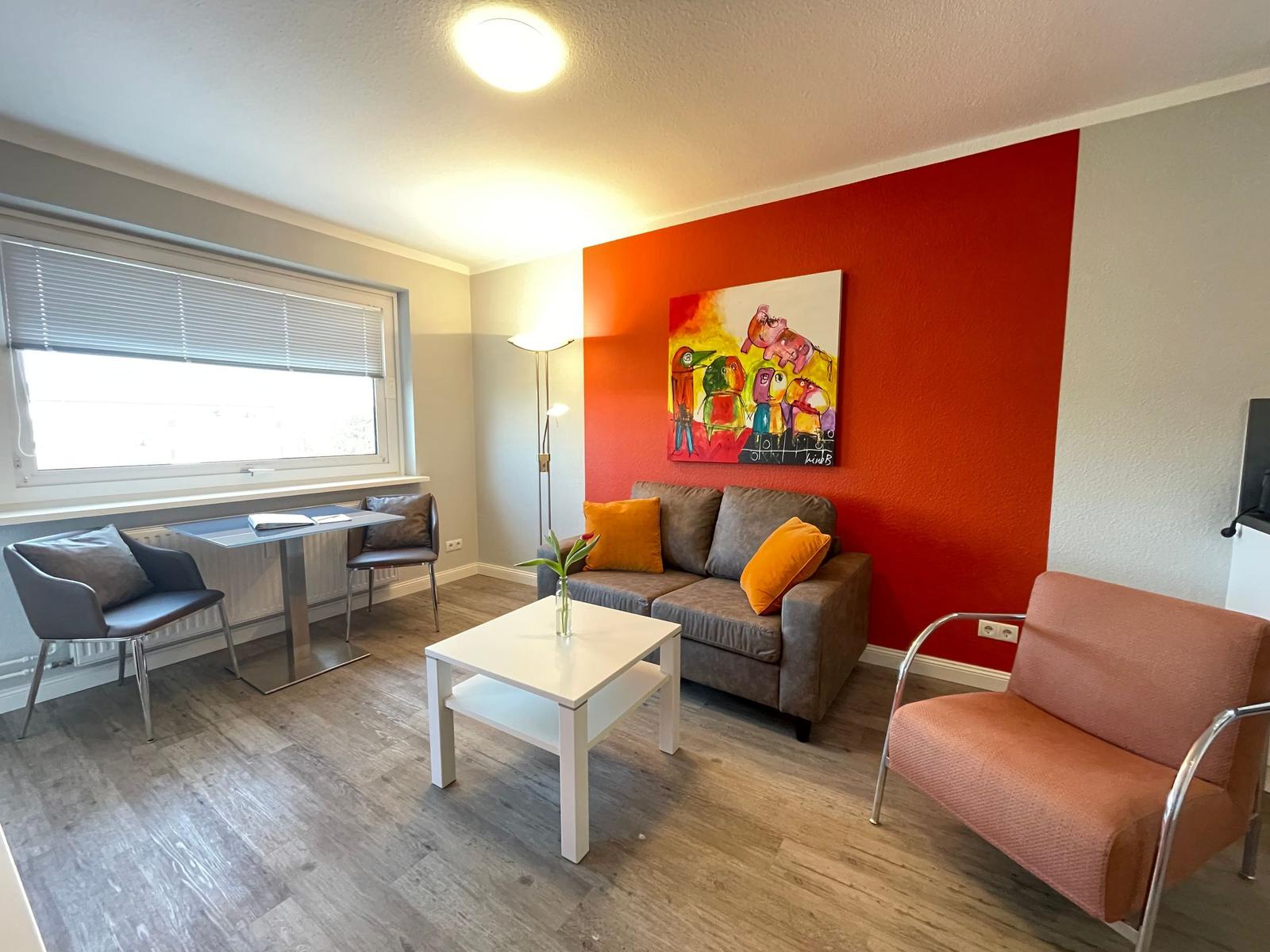 Wohnzimmer mit Sofa, Sessel und Tisch. Wand mit Kunstwerk und Fenster.