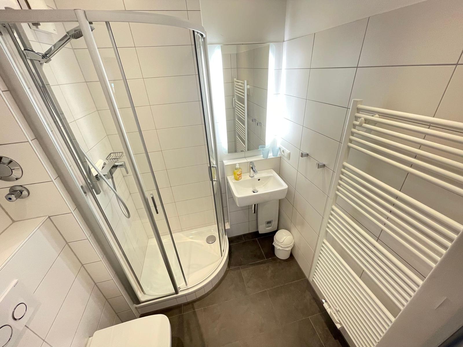 Badezimmer mit Dusche, Waschbecken und Heizkörper