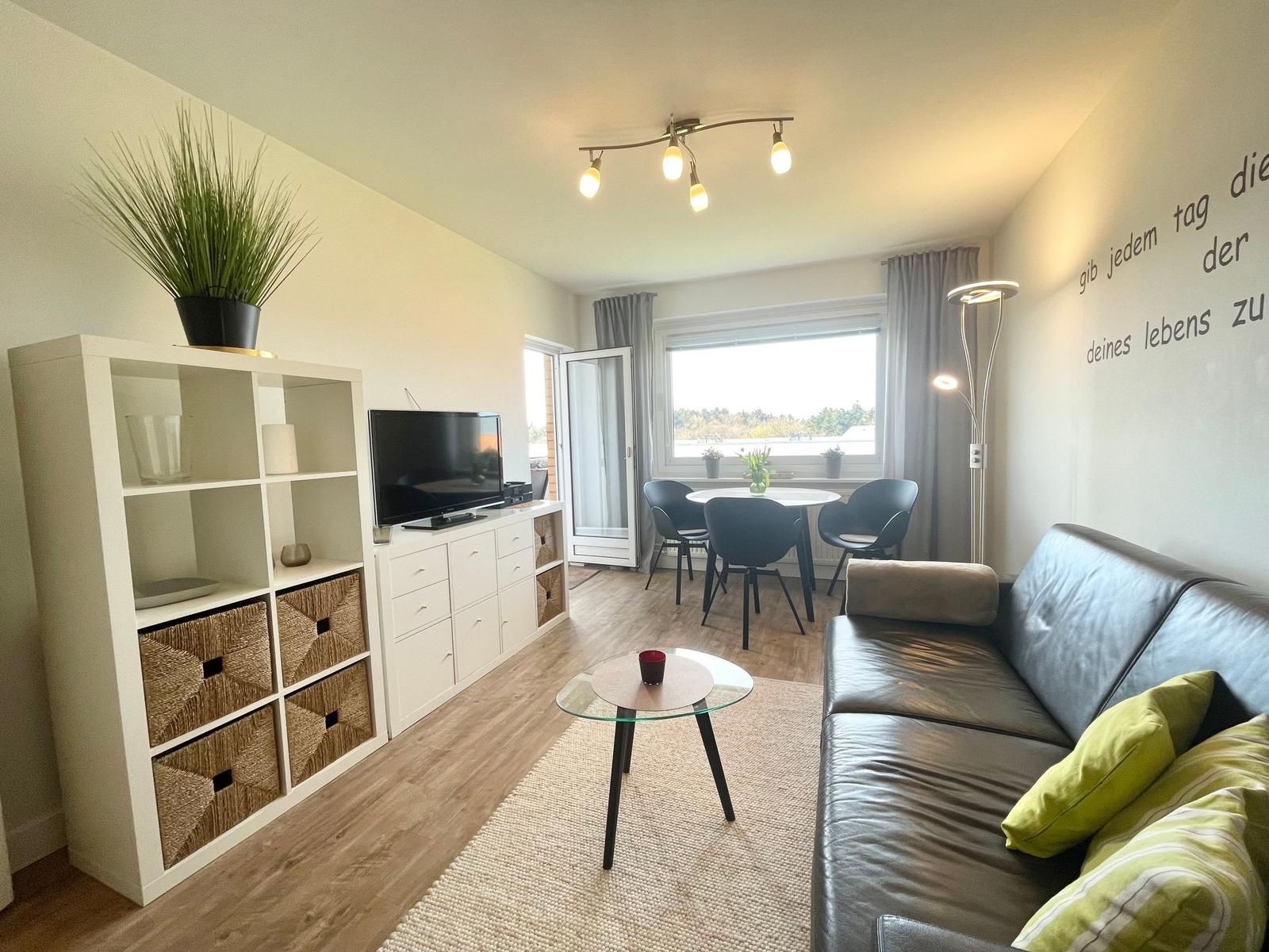 Wohnzimmer mit Sofa, Esstisch und TV. Fenster mit Blick auf Wasser.