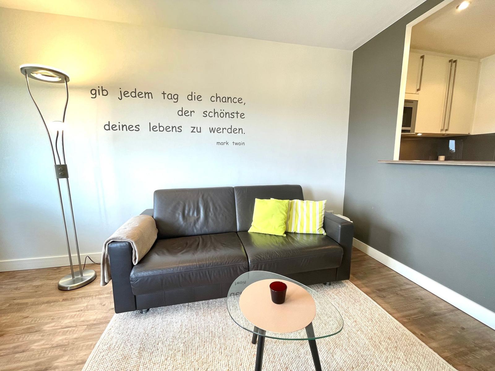 Ein Wohnzimmer mit Sofa, Stehlampe und Wandzitat von Mark Twain.
