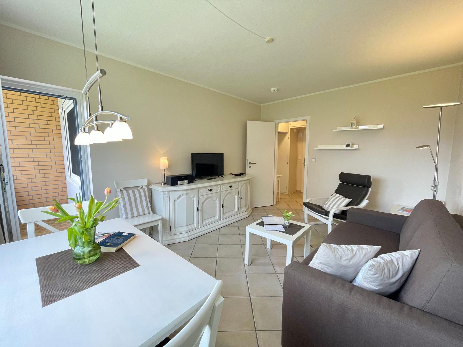 Wohn- und Essbereich mit Sofa, TV-Schrank und Tisch. Terrasse mit Blick auf Backsteinmauer.