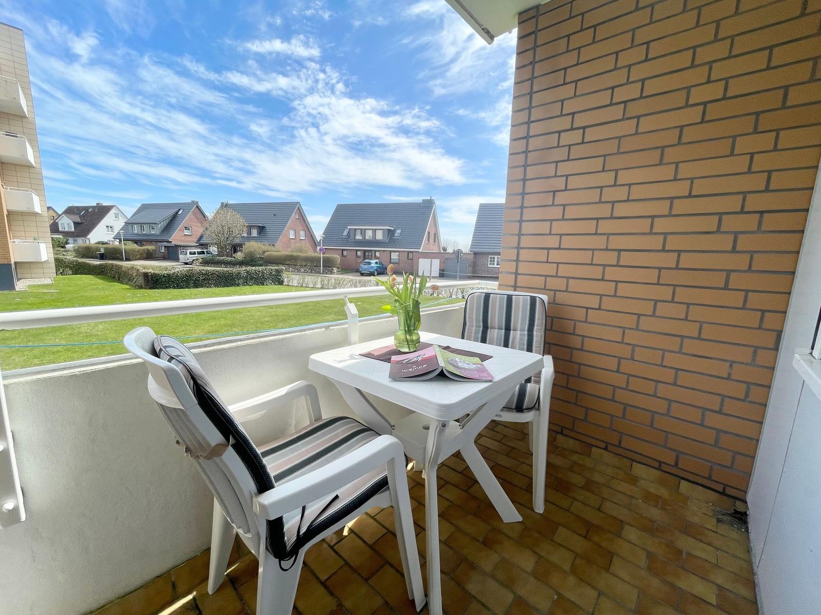 Terrasse mit Tisch und zwei Stühlen, Blick auf Wohnhäuser und Grünfläche.