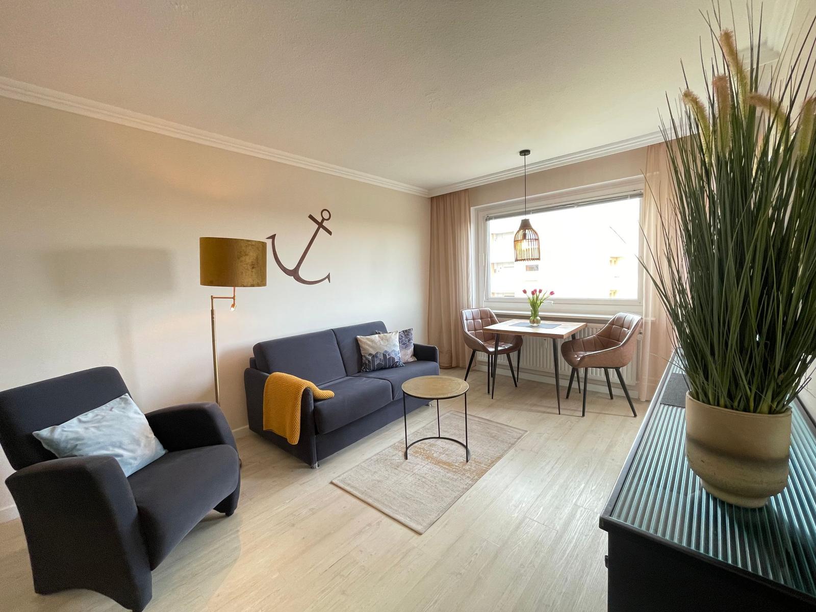 Wohn- und Essbereich mit Sofa, Sessel, Tisch und Stühlen. Wanddekoration und Pflanze sichtbar.