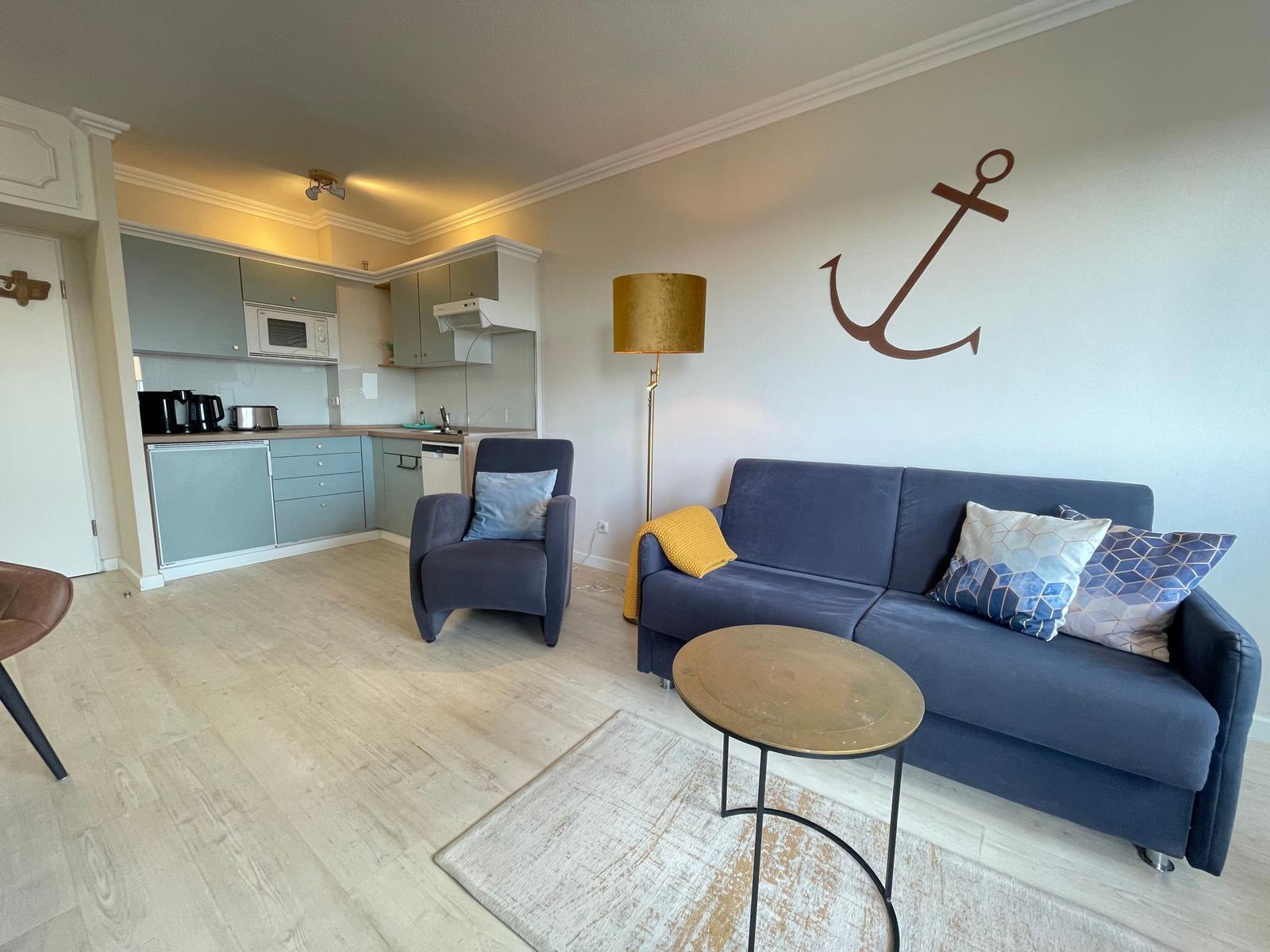 Wohnbereich mit Sofa, Sessel und Küchenzeile. Wanddekoration mit Anker.