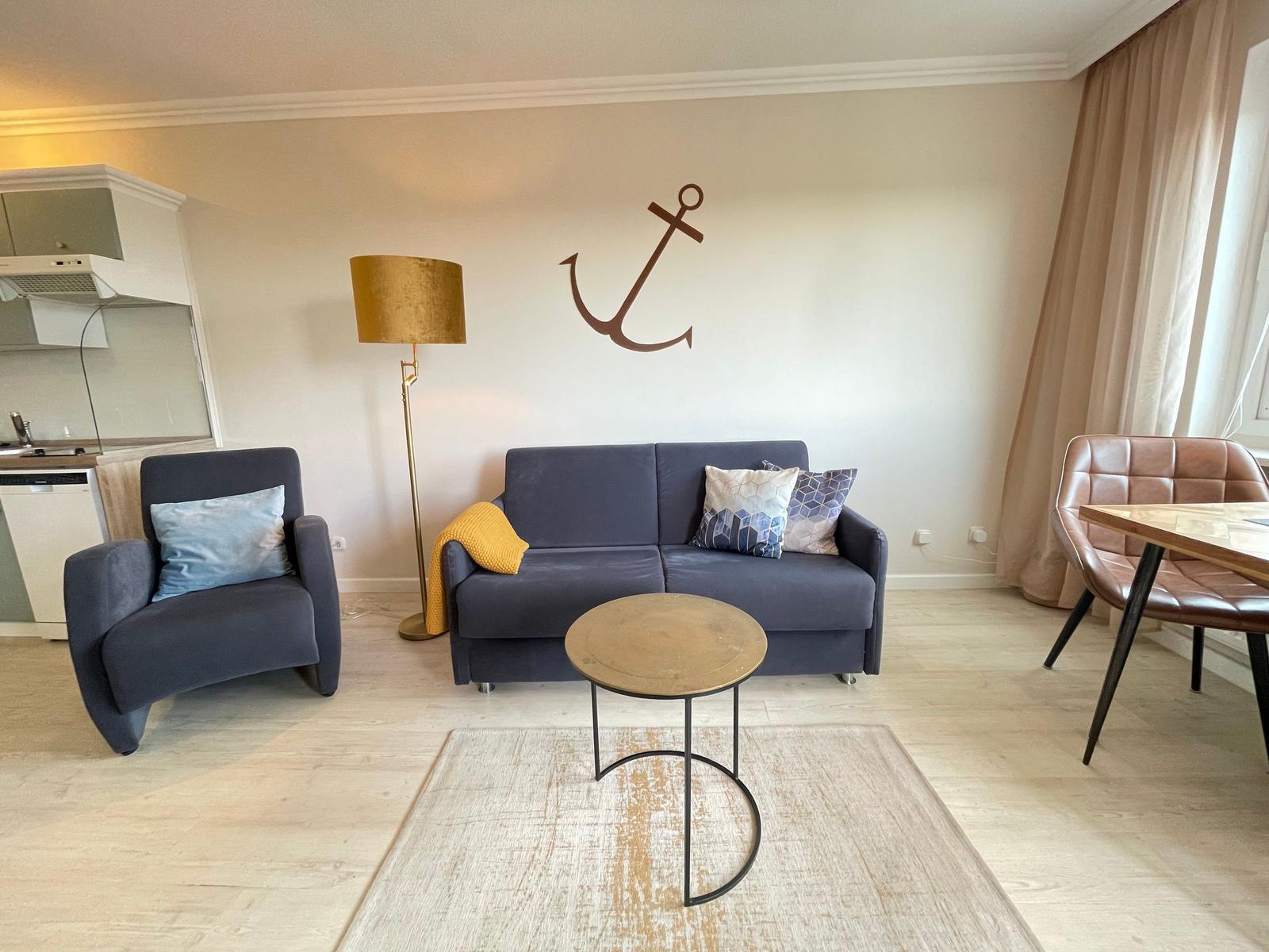 Wohnzimmer mit Sofa, Sessel und Tisch. An der Wand hängt ein Anker.