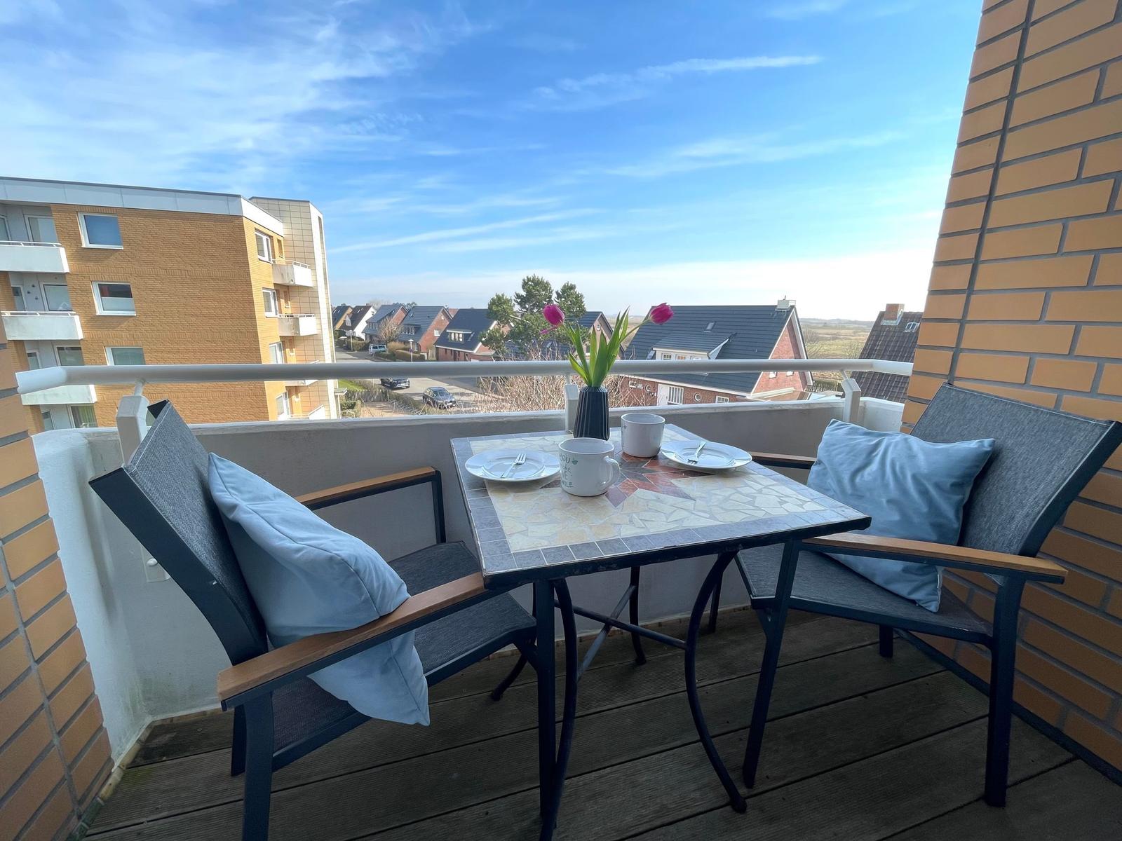Balcony with table, two chairs, and a view of nearby buildings and sky.
