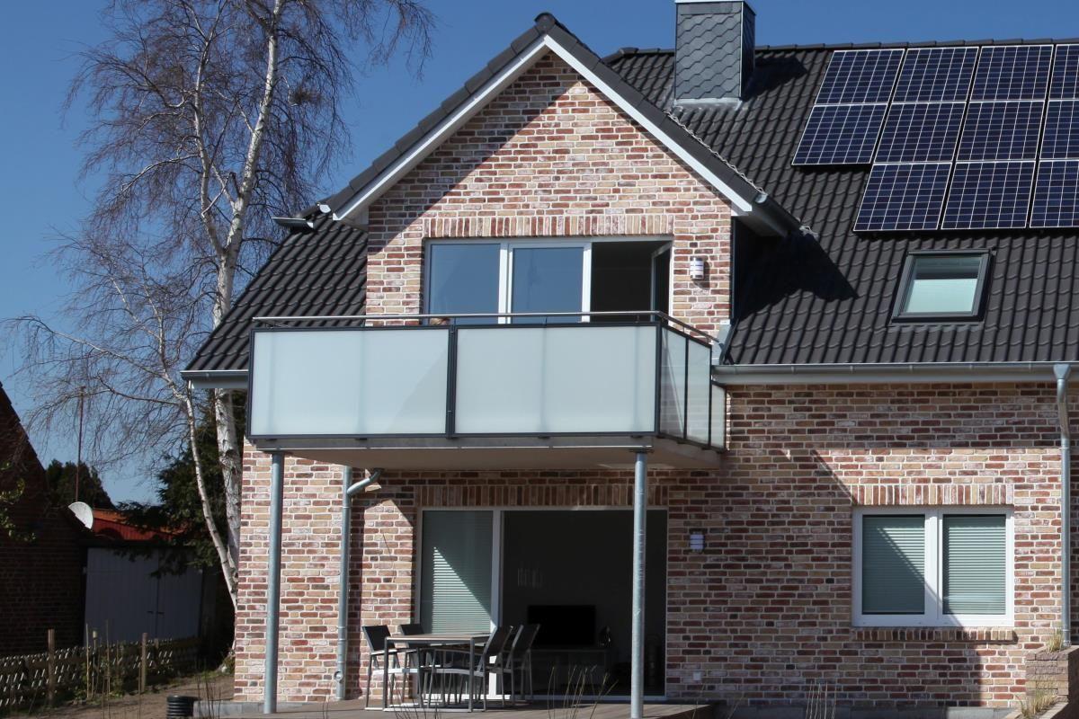 Zweistöckiges Haus mit Balkon, Solaranlage und Terrasse mit Tisch und Stühlen.