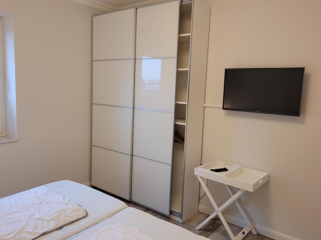 Schlafzimmer mit Doppelbett, Schwebetüren-Schrank und Wand-TV.