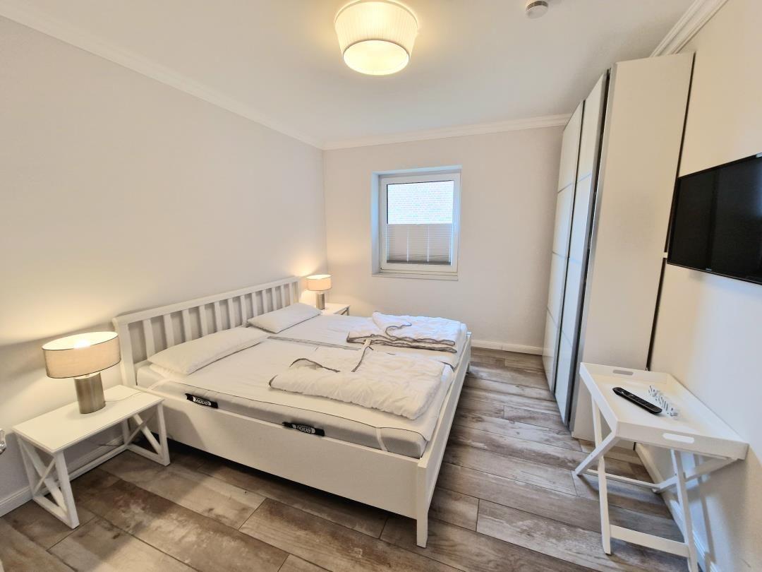 Schlafzimmer mit Bett, Nachttischen, Schrank und Fernseher an der Wand.