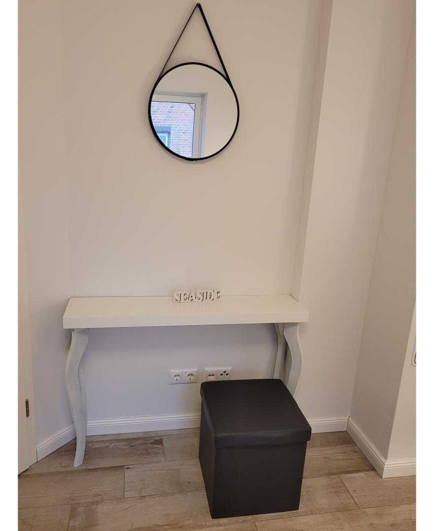 Schmaler Schreibtisch mit schwarzer Sitzbank und runden Spiegel an der Wand.
