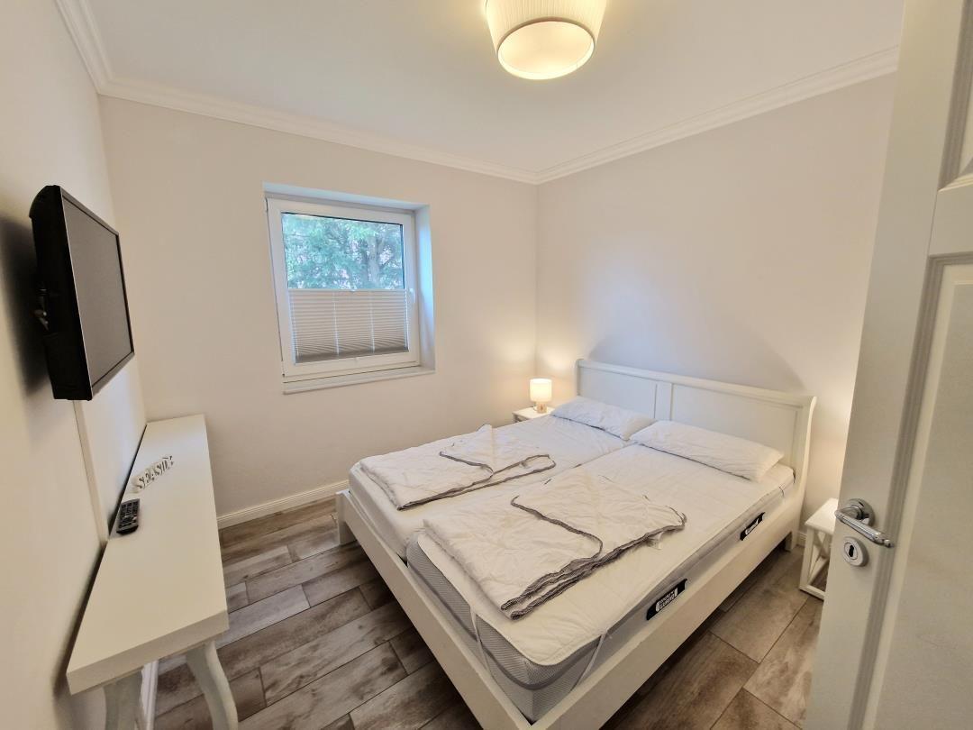 Schlafzimmer mit Doppelbett, Fenster, Schreibtisch und Fernseher.