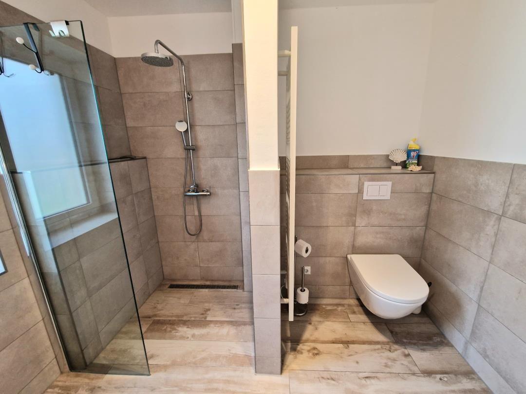 Badezimmer mit Dusche, Toilette und Fliesenboden.