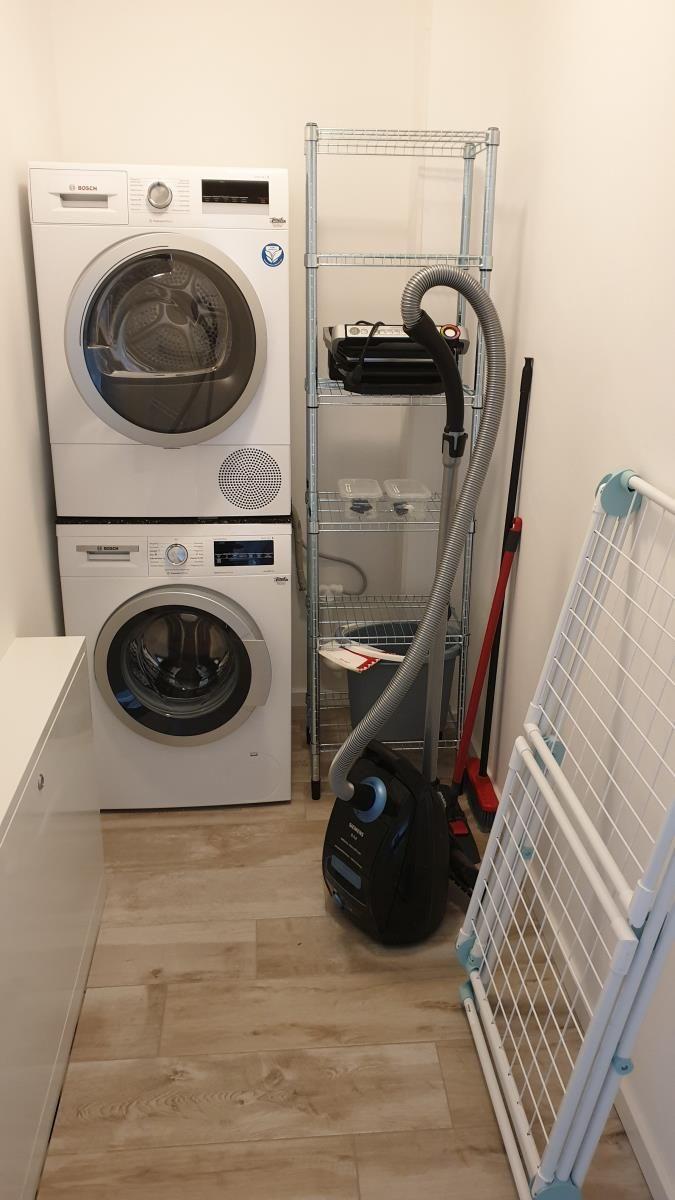 Wäschetrockner und Waschmaschine in einem Raum mit Stahlregal und Staubsauger.