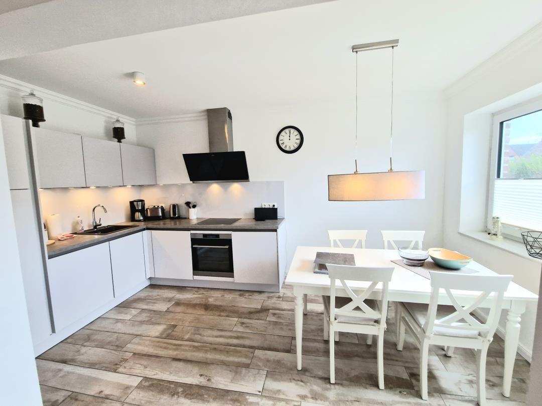 Moderne Küche mit Essbereich. Weiße Möbel, Holzboden und Fenster.