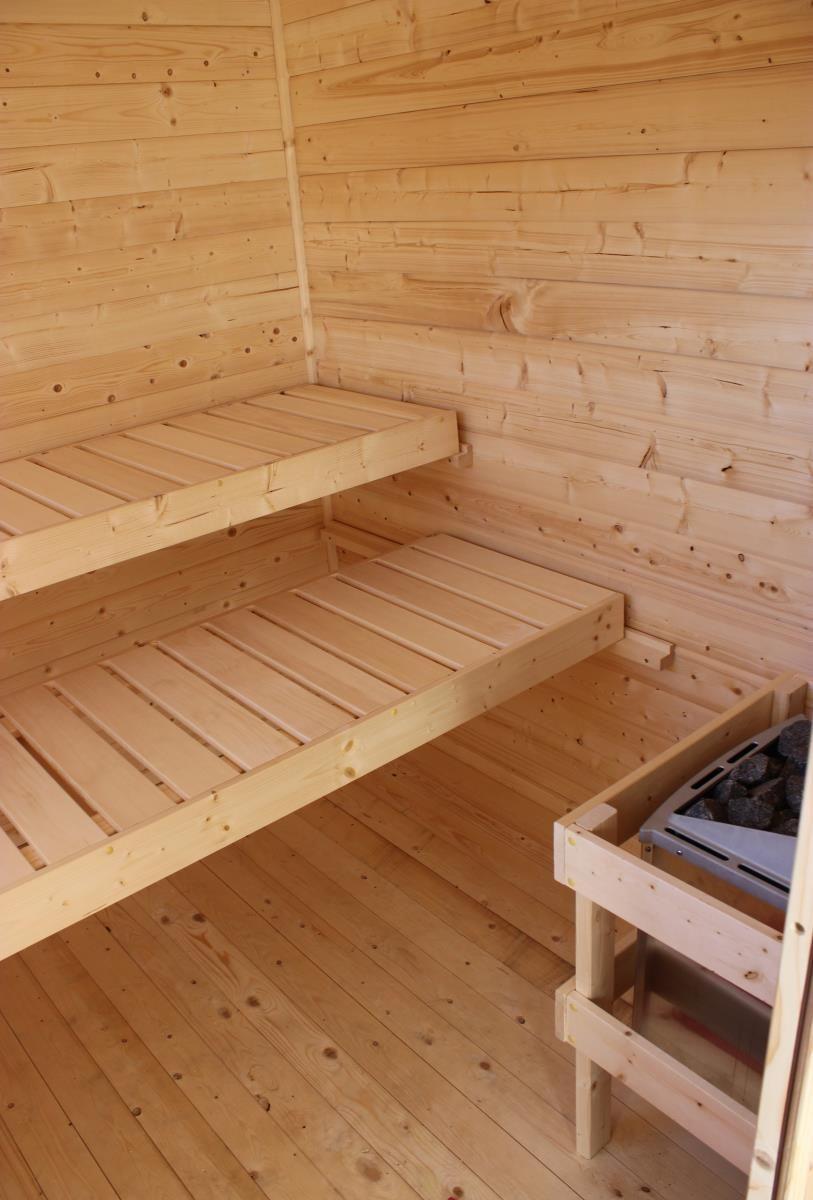 Sauna mit Holzbanken und Holzwandverkleidung. Im Vordergrund ist ein Holzofen mit Steinen zu sehen.