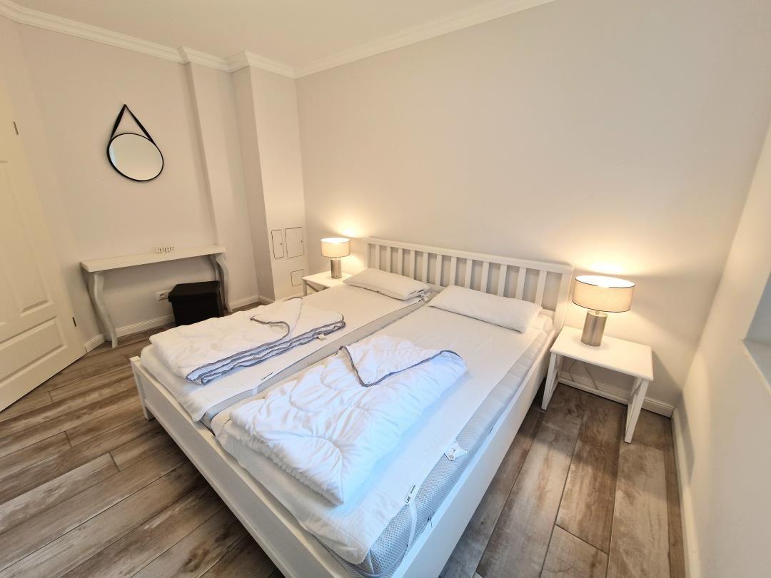 Schlafzimmer mit Doppelbett, zwei Nachttischen und einem Spiegel an der Wand.