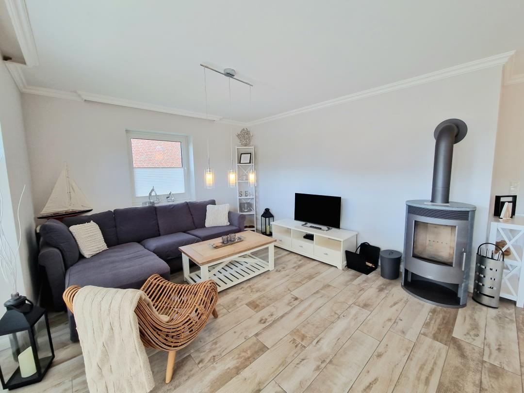 Wohnzimmer mit Sofa, Kaminofen und Holzboden. Fernseher und Couchtisch sichtbar.