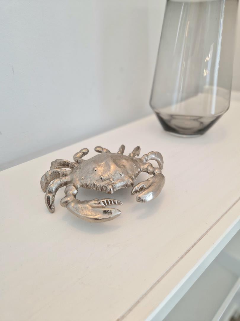Ein silbernes Krabbenobjekt steht auf einer weißen Oberfläche neben einem Glasvasen.