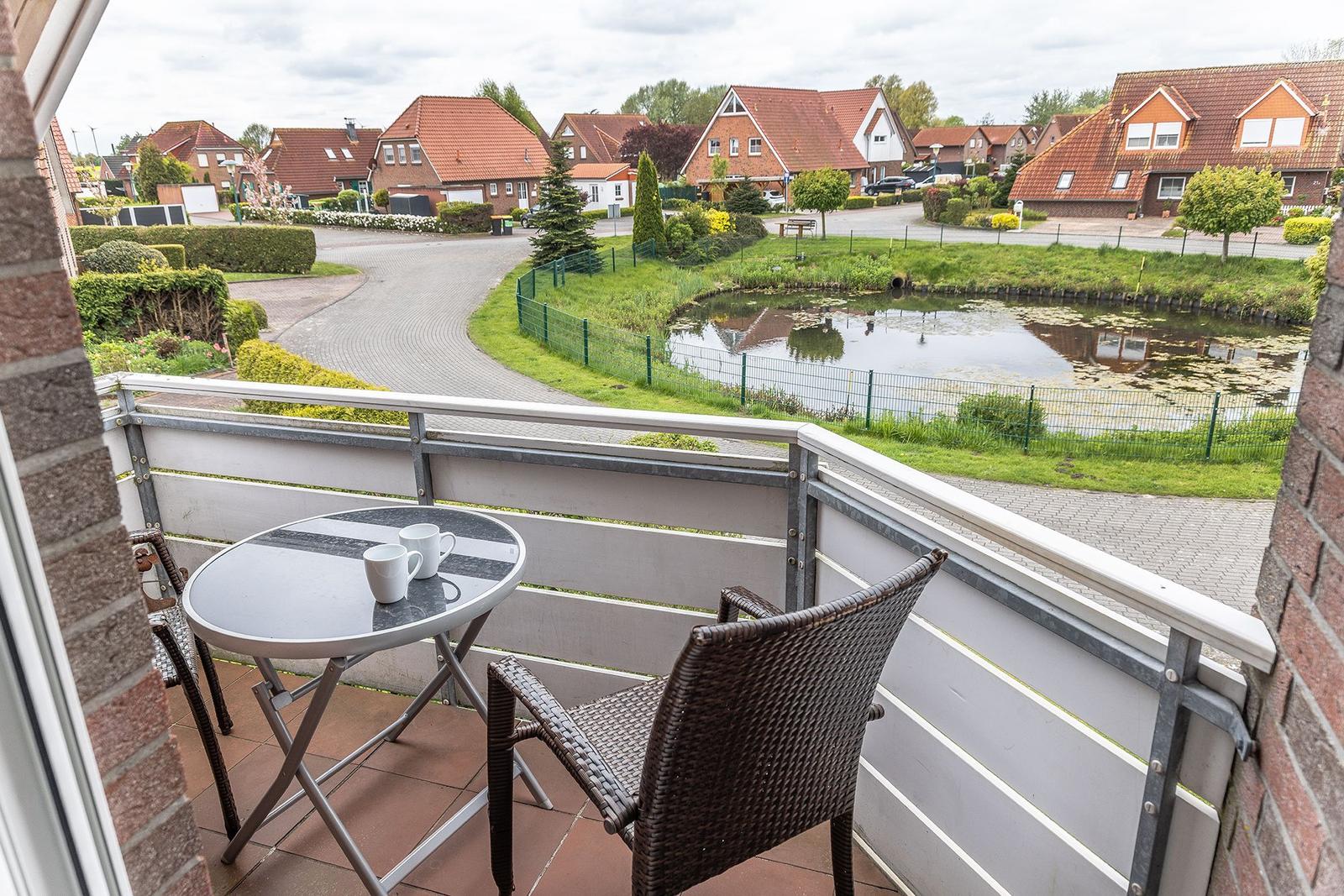 Balkon mit Tisch und Stühlen, Blick auf einen Teich und Wohnhäuser.